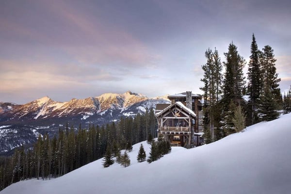 Mountain view house set on a hillside perfect for skiing. In the background is a beautiful mountain scene as the sun is starting to set.