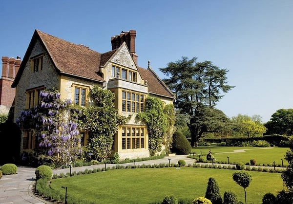 An old-English house featuring a central gable with gridded windows sitting on a green lawn with clear blue skies in the background.