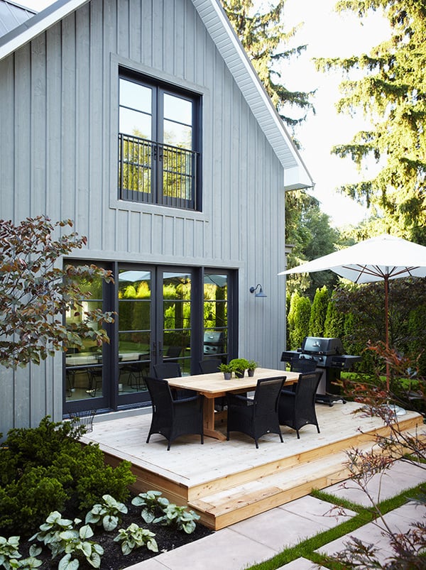 A light blue board and batten home with modern windows and beautiful modern backyard landscaping