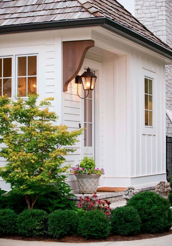 A coastal home with white board and batten, beautiful black sconces, and wooden corbels