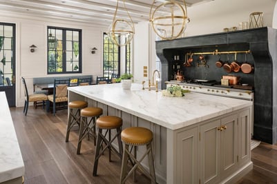 A new kitchen with marble countertops, black grid windows, a dining nook, and a large gas range with brass knobs.
