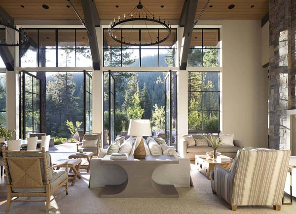 Beautiful interior of a mountain house with large open windows that bring in sunlight and fresh air into a living room with mountain home decor. 