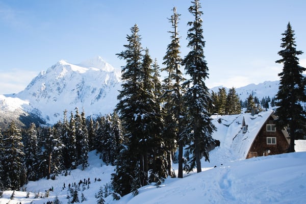 A mountain home that mimics the style of a adirondack cabin covered in snow with a beautiful mountain view in the background.