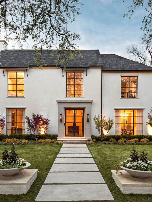 A cement pathway on a green landscaped lawn leading toward a gray stucco home with transitional windows&nbsp;