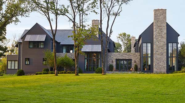 A black transitional farmhouse with metal siding, tall windows, and a stone chimney