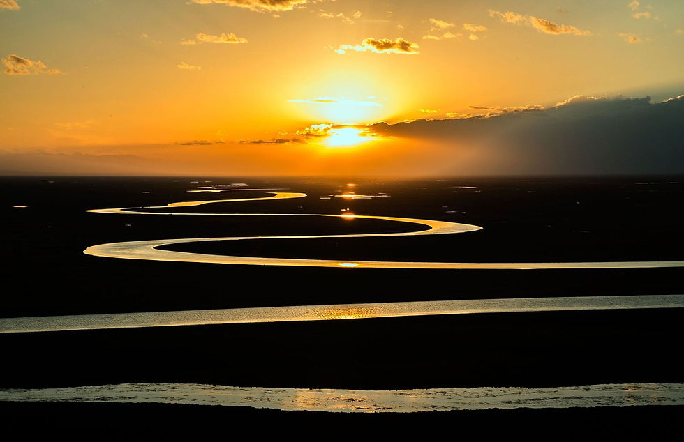 This is a picture of a sunset illuminating a winding river. The sky is a golden color, and there are a few clouds in the sky. 