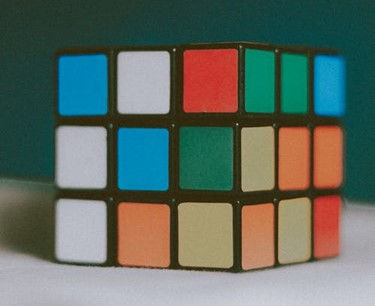 This is a picture of an unsolved Rubik's cube sitting on a flat surface.