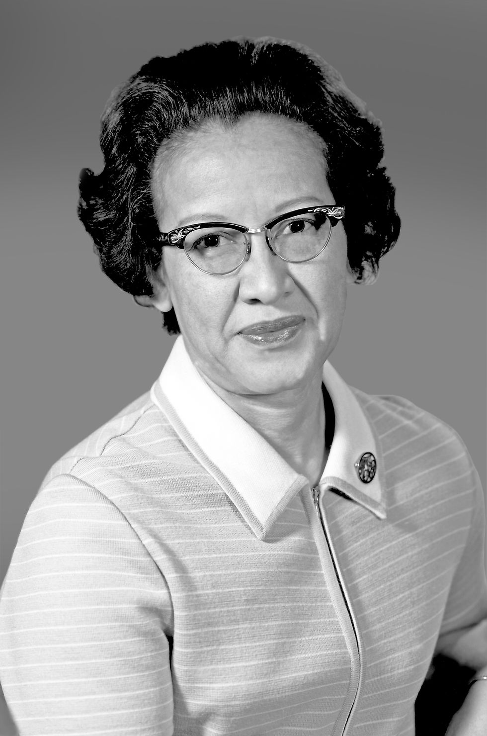 This is a black-and-white portrait of Katherine Johnson, a Black woman with short, black hair. She's wearing glasses and a light colored, striped, collar shirt.