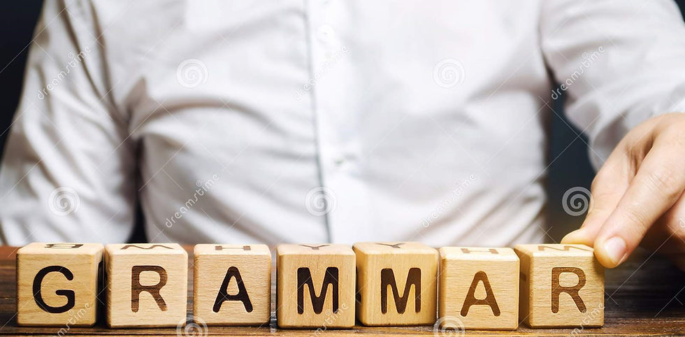 This is a picture of a man sitting at a table. In front of him are some wooden blocks that spell out the word "grammar."