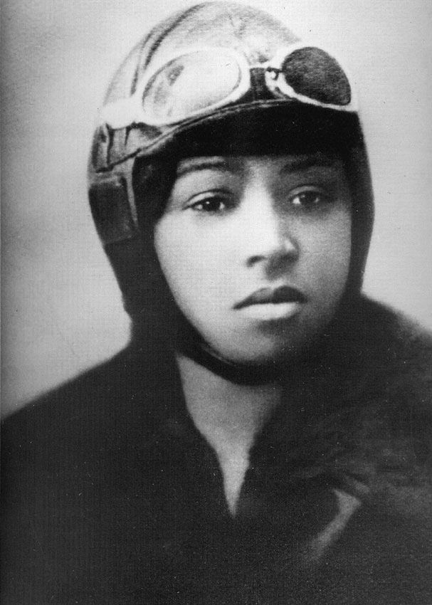 This is a black-and-white portrait of Bessie Coleman, a Black woman. She's wearing an aviator hat, goggles, and a bomber jacket.