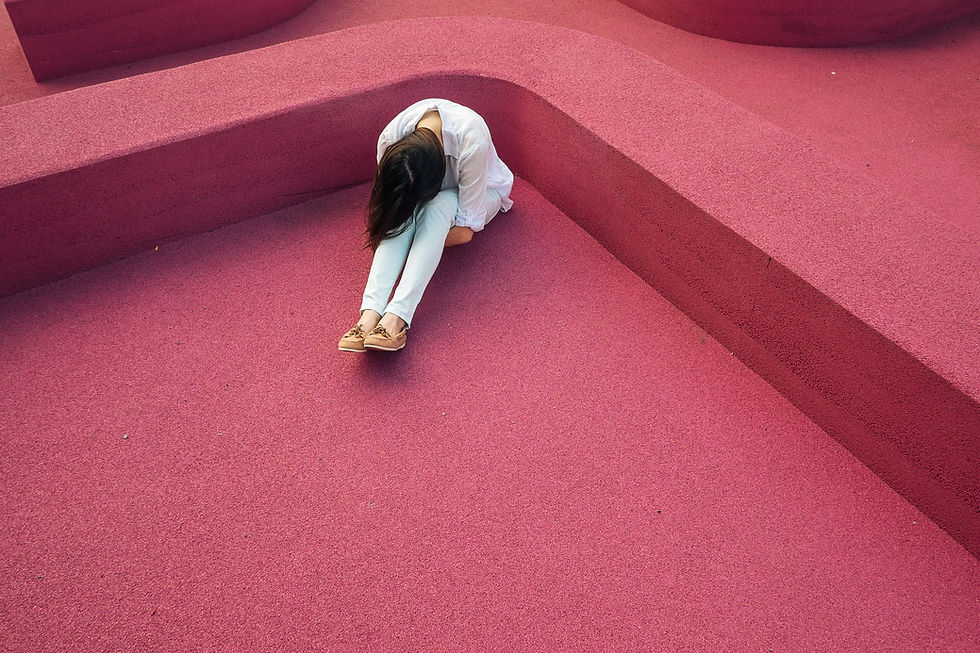 This is a picture of a woman sitting on a red floor. She has her head in her knees, and she has her arms wrapped around her thighs, as if she's emotionally overwhelmed.