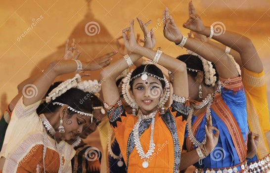 This is a picture of four young Indian women who are dressed in traditional clothes. They're wearing traditional clothes. Their arms are in the air, and their wrists are crossed above their heads. 