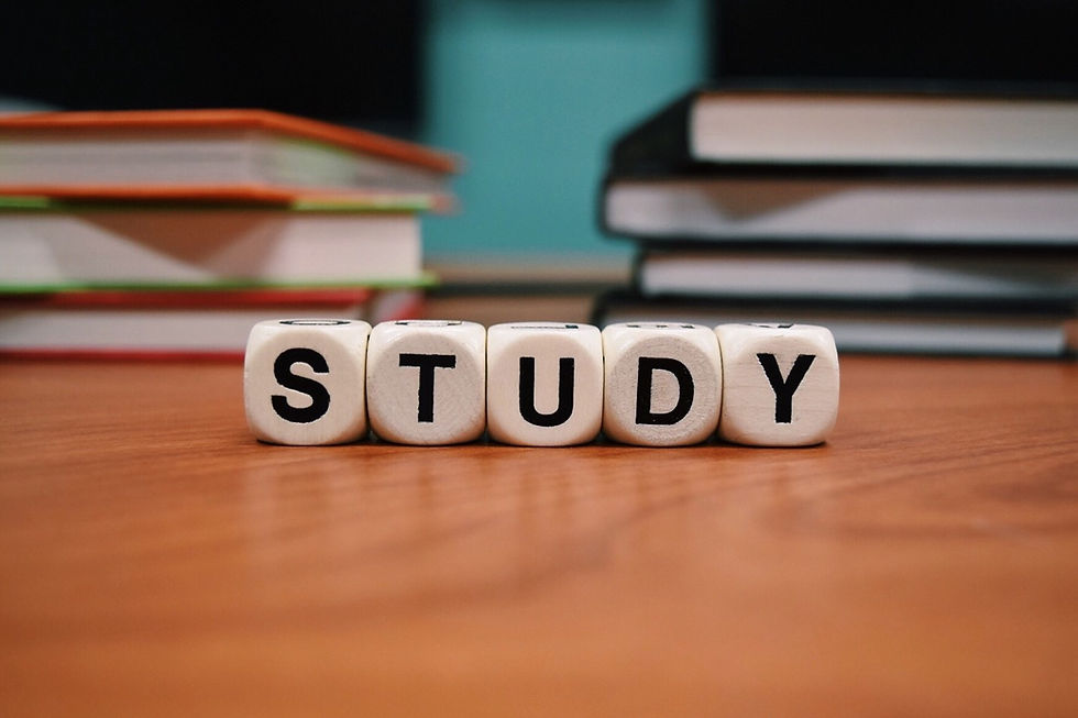 This is a picture of five blocks sitting on top of a wooden desk. The blocks spell out the word "study," and there are stacks of books behind them. 