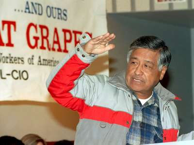 This is a picture of Cesar Chavez, an older Latino man, in front of a banner. 