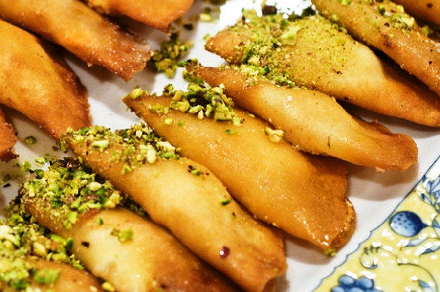 This is a picture of a tray of Qatayef with crushed pistachios sprinkled on top. 