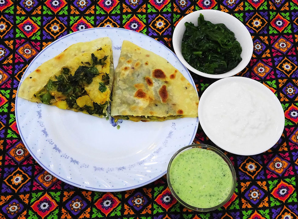 This is a picture of two slices of Bolani on a plate. Near the plate are three small bowls. One has cooked greens, one has a white dip, and one has a green dip.