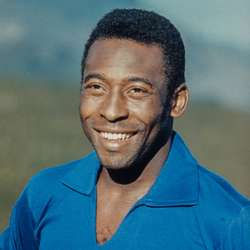 This is a picture of Pelé, a smiling Black man. He has short, black hair, and he's wearing a blue shirt. He's only visible from his head to his shoulders.