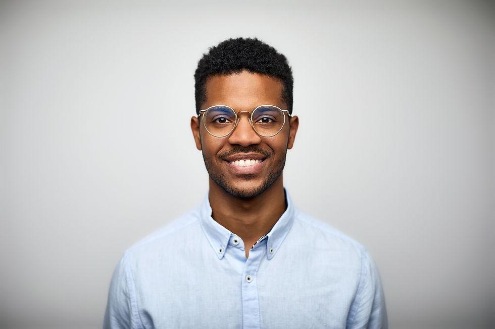 There is a young Black man against a white background. He has short dark hair, and he's hearing glasses and a light blue shirt.