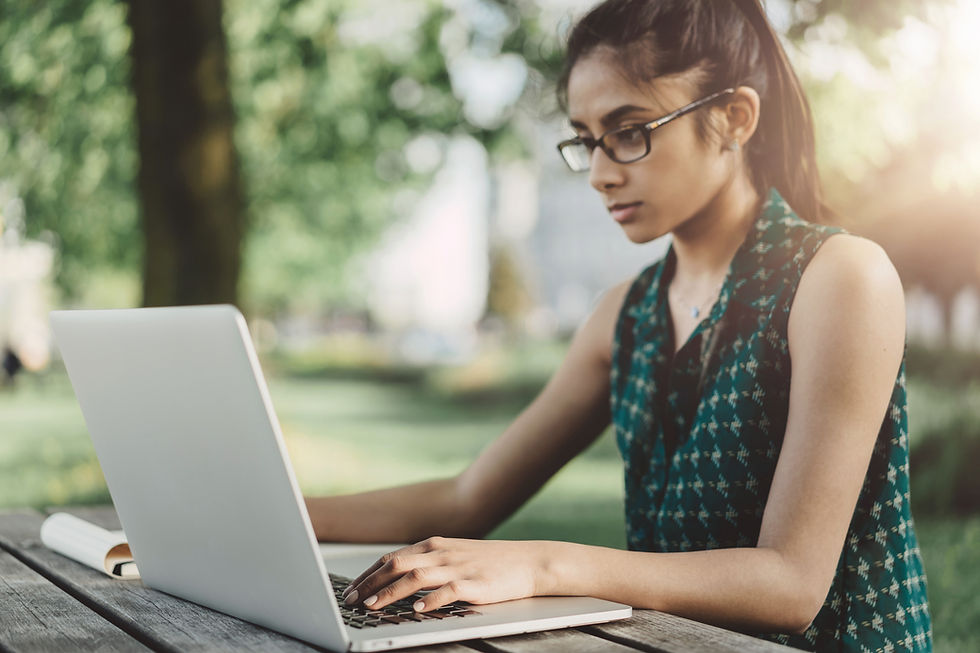This is a picture of a student sitting at a picnic table on her laptop.