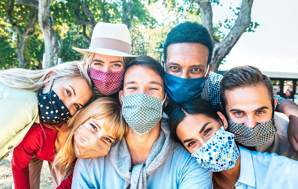 This is a picture of seven people of different races crowded together. All are wearing cloth masks over their faces. There are three white women, one white man, one asian man, one asian woman, and one Black man. 