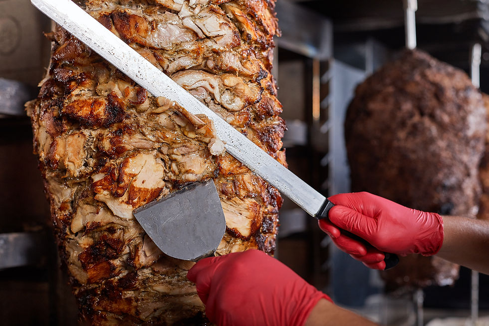 This is a picture of cooked Shawarma on a rotating cone. There are a pair of hands that are cutting the Shawarma, and they hands are wearing red disposable gloves. 