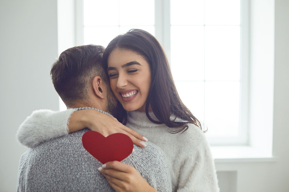This is a picture of a man and a woman hugging each other. The woman is holding a red paper heart. 