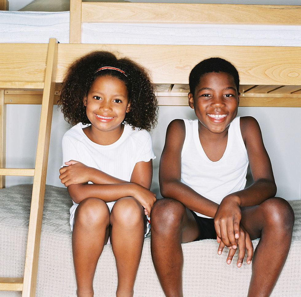 Two African-American children, a boy and a girl, are sitting next to each other on the bottom bunk of a bunk bed. 
