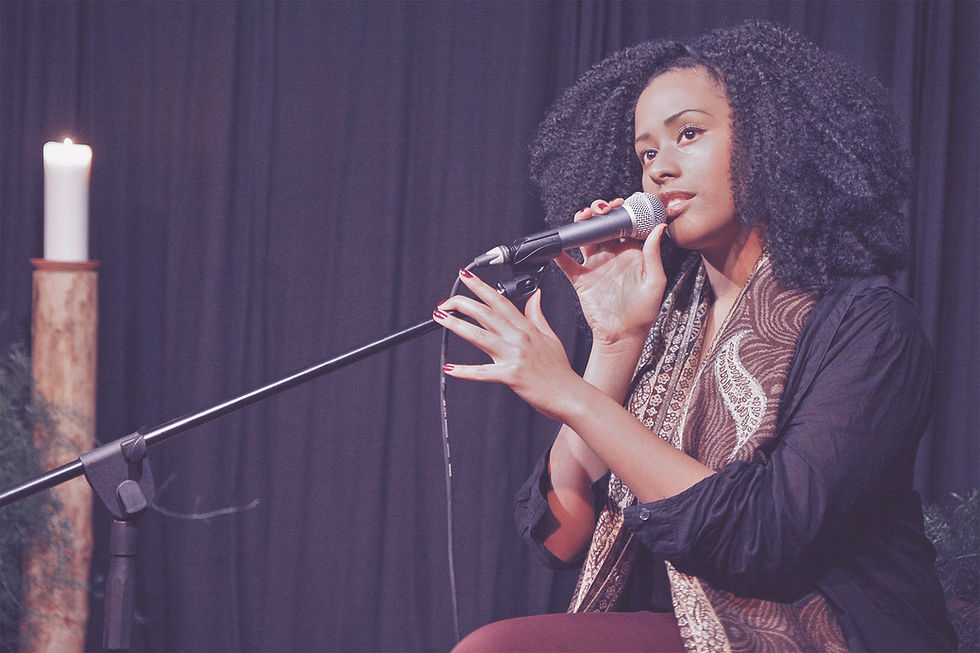 This is a picture of a Black woman sitting on a stage holding a microphone. 