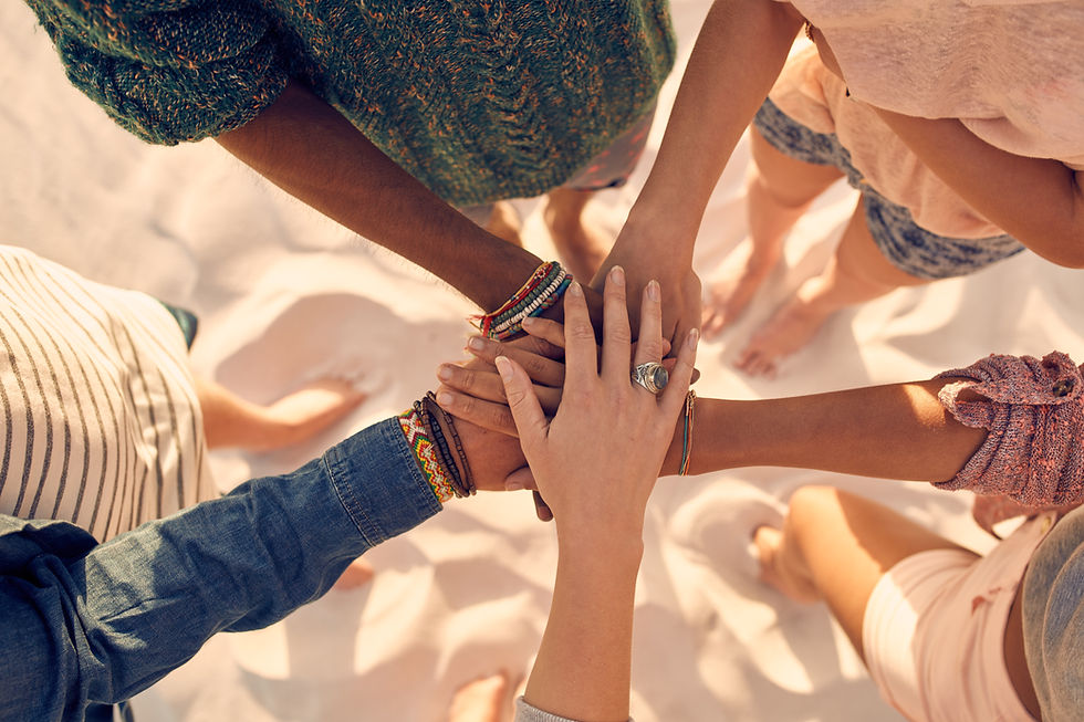 This is an overhead shot of five children of different races standing in a circle. The children have their outstretched hands piled up in the middle.