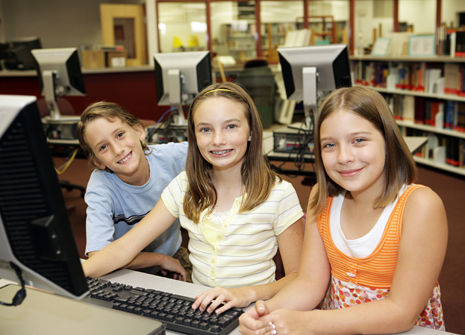 This is a picture of a boy and two girls sitting in front of a computer.in a library.