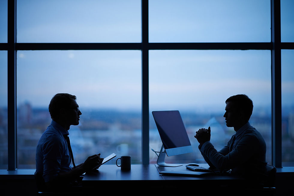 This is a picture of the silhouettes of two businessmen. They're sitting at a desk besides a large window.