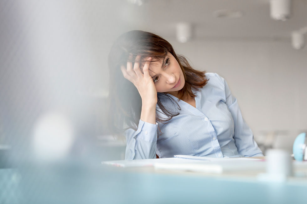 This is a picture of a woman sitting at a desk. She has brown hair, and she's wearing a blue, long-sleeved shirt. She's holding her head in her hand, as if she's overwhelmed.