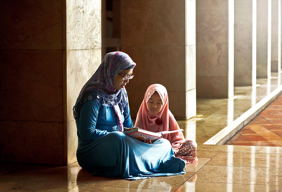This is a picture of a mom and daughter sitting on a marble floor, reading a book together. Both are wearing hijabs. 