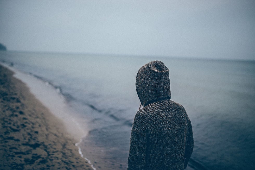 This is a picture of a teenage boy wearing a gray hoodie, walking down a beach. 