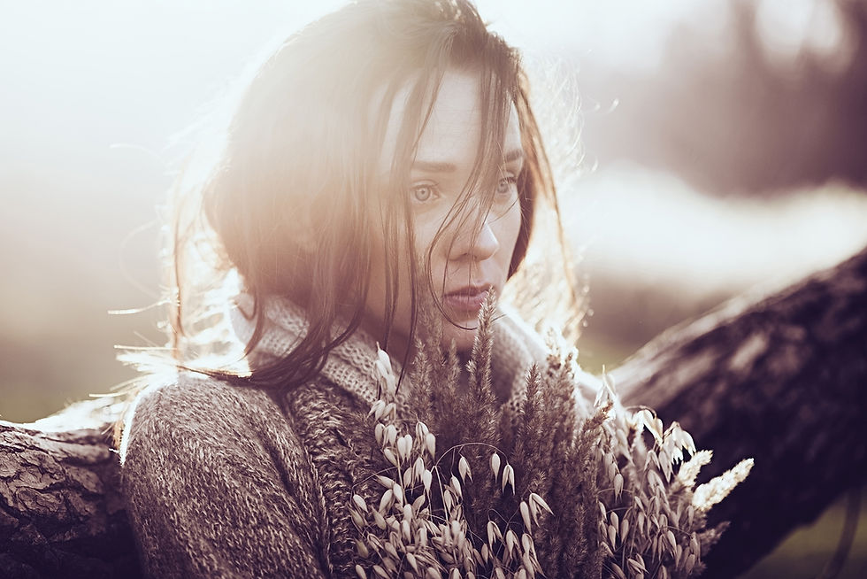 This is a picture of a sad woman leaning by a tree. She's wearing a sweater and holding flowers, and she's staring off into the distance. 