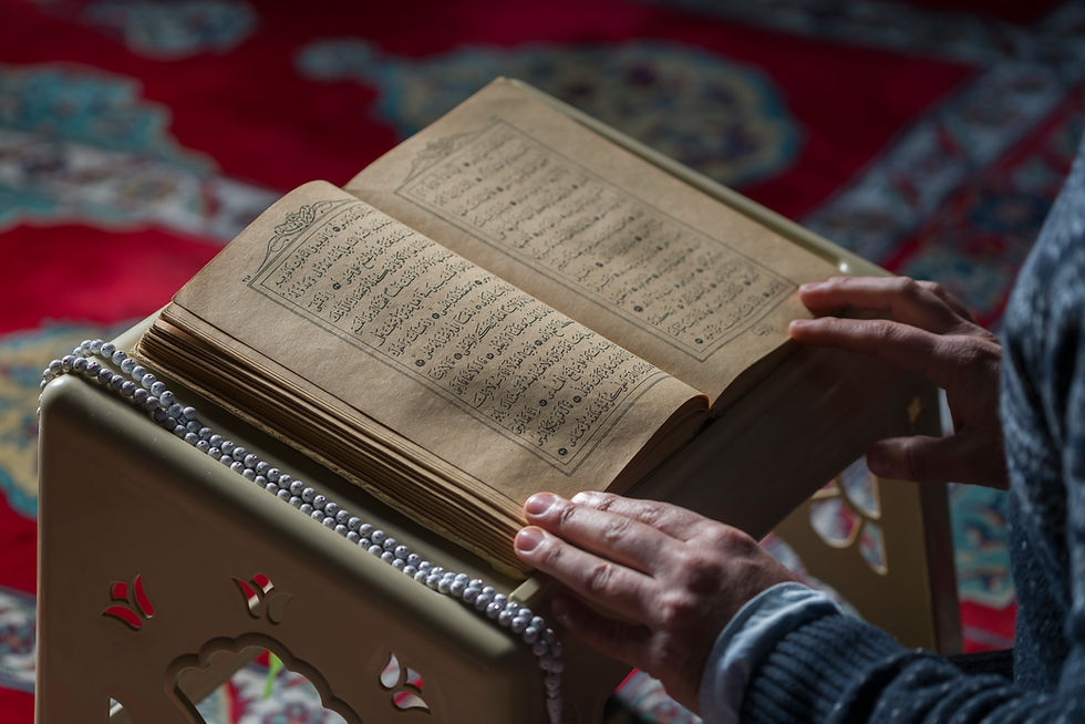 This is a picture of an open Quran resting on a podium. There are two hands resting on it, as if to keep the book open. 