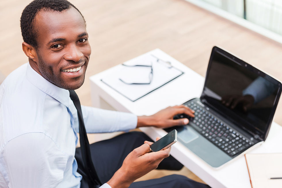 African-American man typing on a laptop to practice his Business English while smiling at the camera
