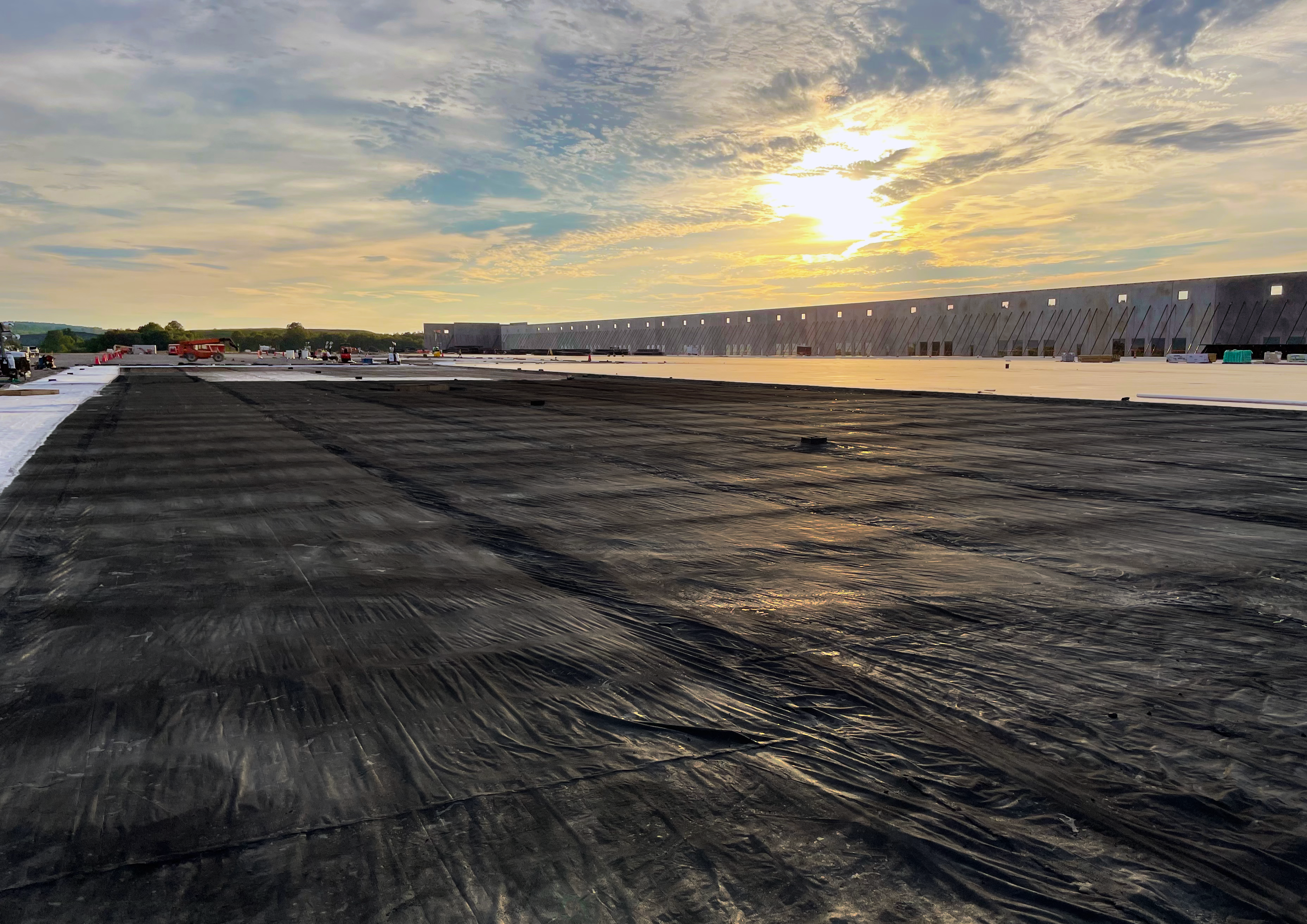 A job site at sunset is pictured. There is a work crew in the distance.