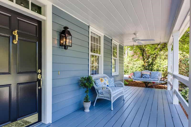 A front porch at an angle with a dark brown door on the left of the frame. The siding and porch are…