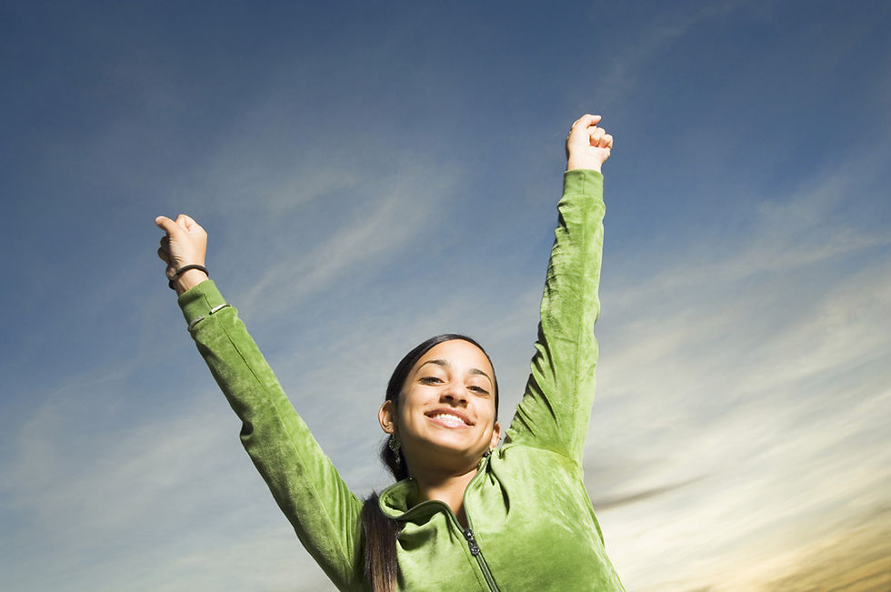 The image shows a young woman against a background that looks like the sky. She has her hands in fists, her arms are stretched into a "V" over her head, and she's smiling.