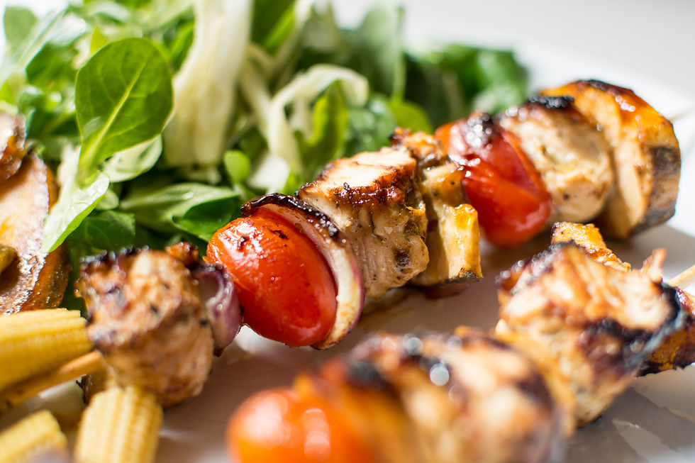 This is a picture of a plate with shish kebabs and a salad. The shish kebabs have grilled chicken, tomatoes, and onions. 