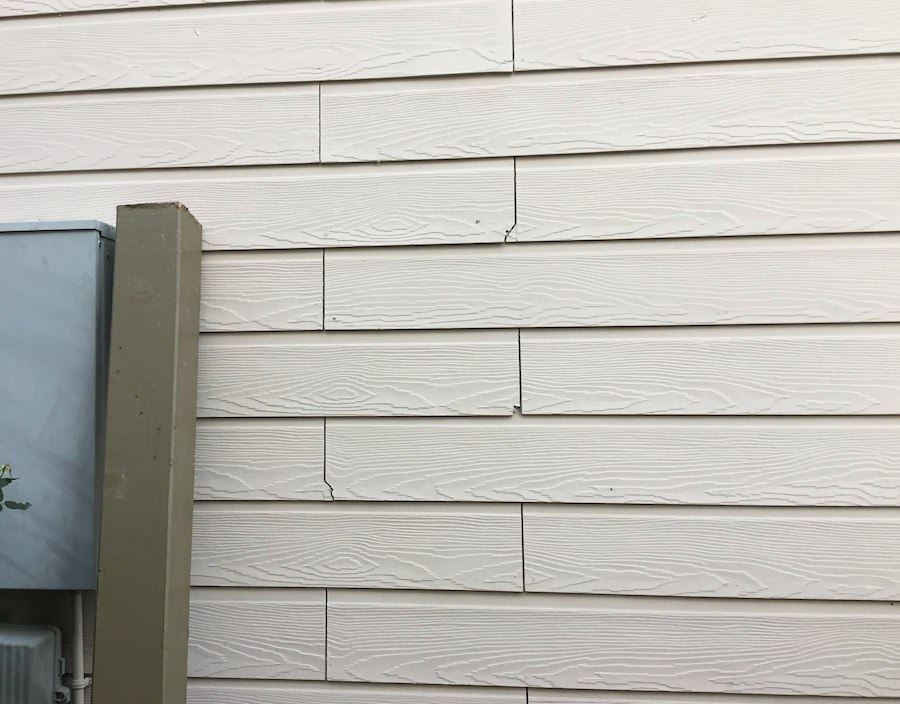 A close-up of white siding shows cracks in two separate planks.